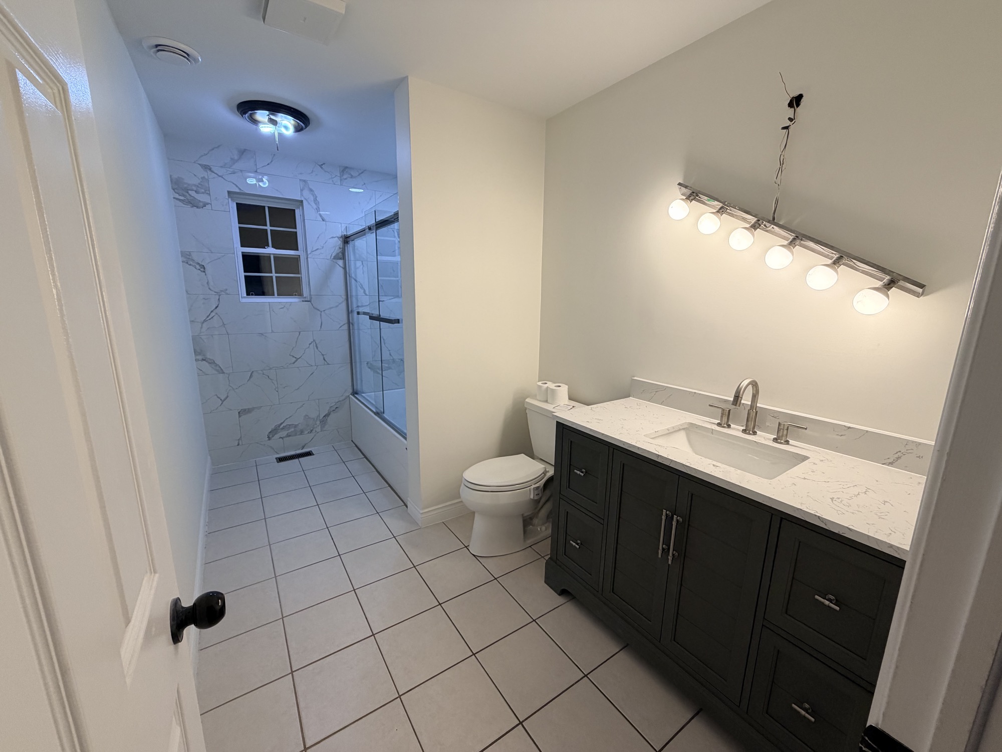Completed bathroom renovation with dark vanity and tile shower.